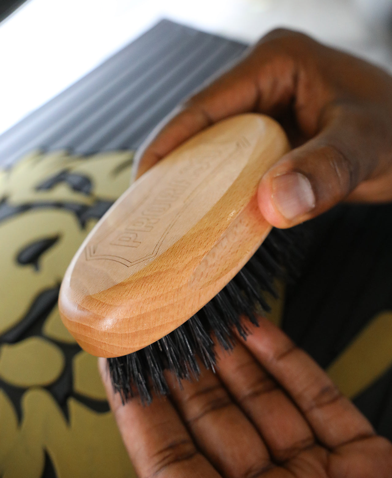 Man holding the Old Style Military Brush bristles down for a closeup of the wooden handle over a barber counter