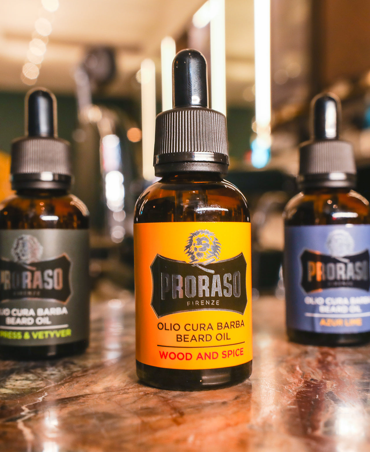 Lineup of Beard Oils from left to right, Cypress & Vetyver, Wood & Spice and Azur Lime sitting on a dark brown marble take with a barbershop in the background. 
