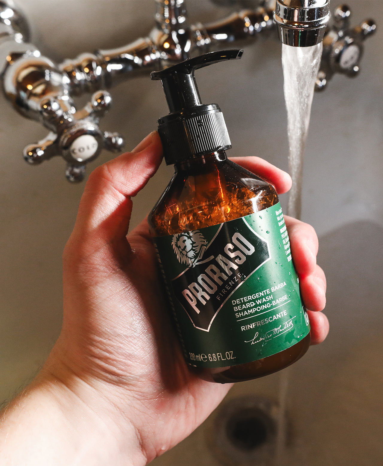 Man holding Refresh Beard Wash in front of a vintage sink with the water running in background