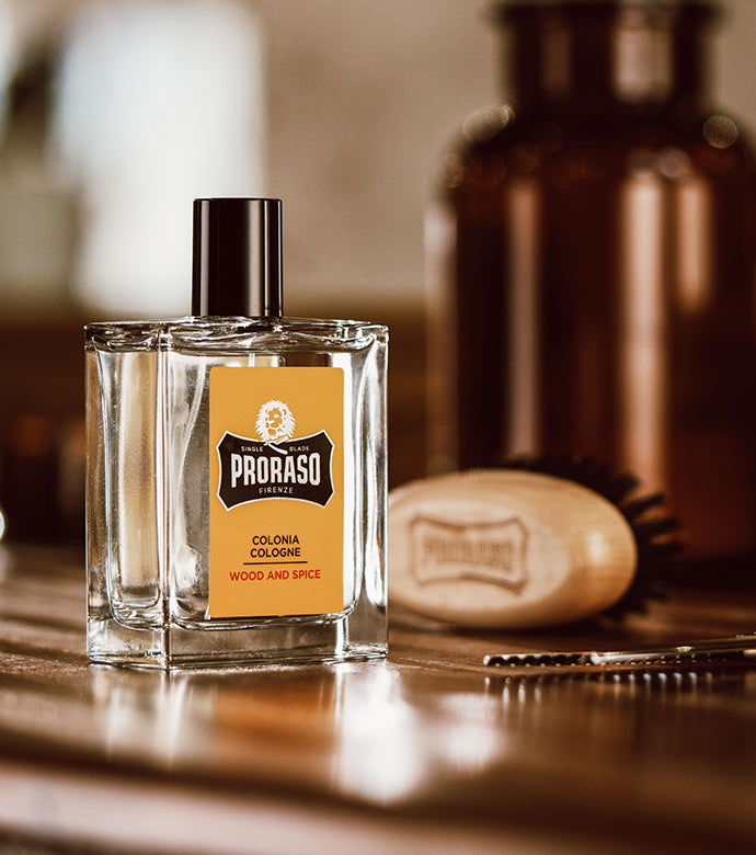 Wood & Spice Cologne sitting on a brown wooden table with a Moustache and Beard Brush sitting in the background with a pair of scissors 