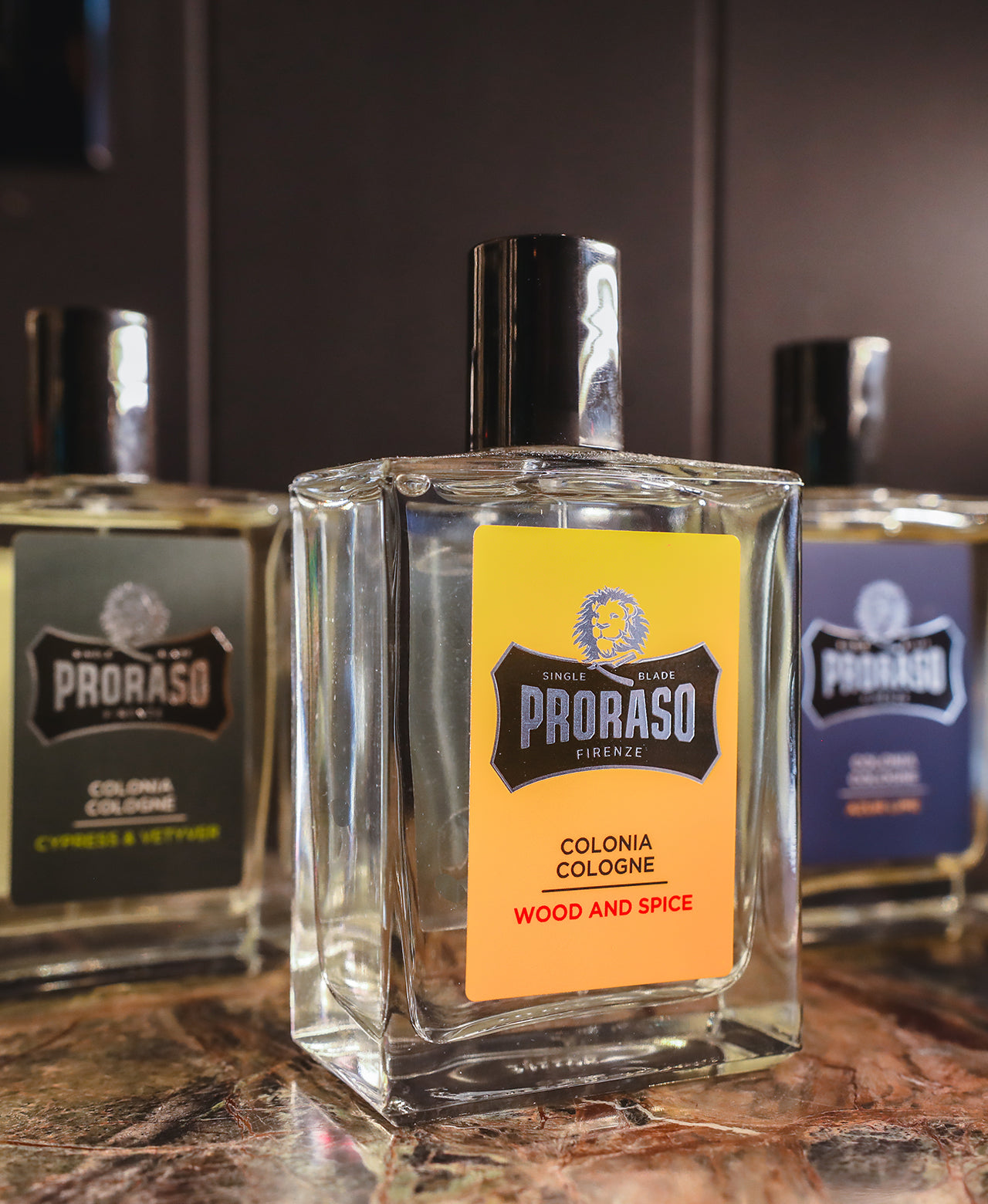 Left to right Cypress & Vetyver, Wood & Spice and Azur Lime Cologne sitting on a dark brown marble table with black wooden background