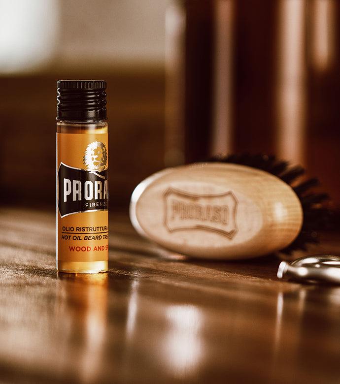 Hot Oil Beard Treatment single Vial sitting on brown wooden table with Moustache and Beard Brush in the background