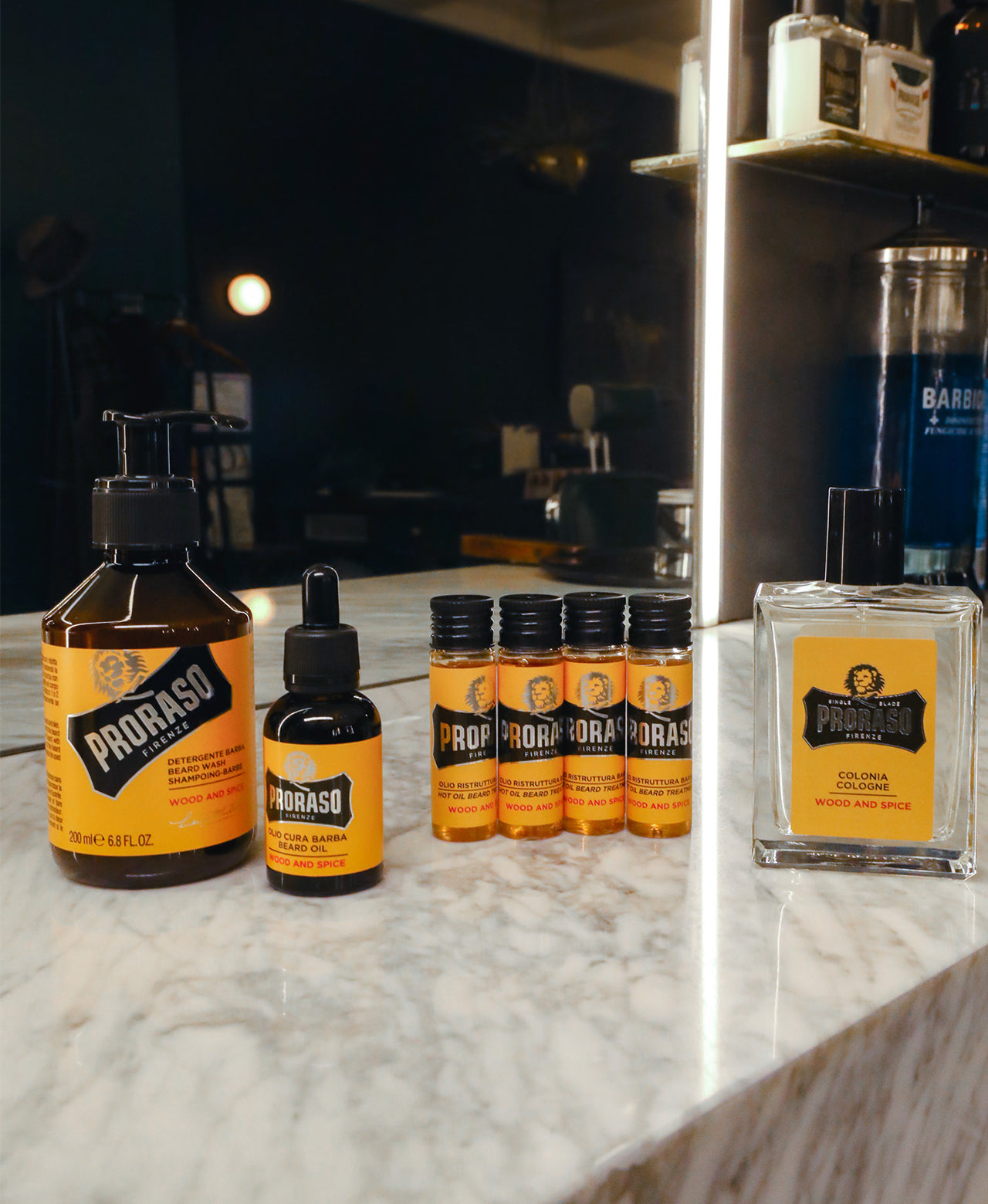 Wood & Spice Beard products left to right Beard Wash, Beard Oil, Hot Oil Beard Treatment and Cologne sitting on a white marble barber counter with mirror in the background