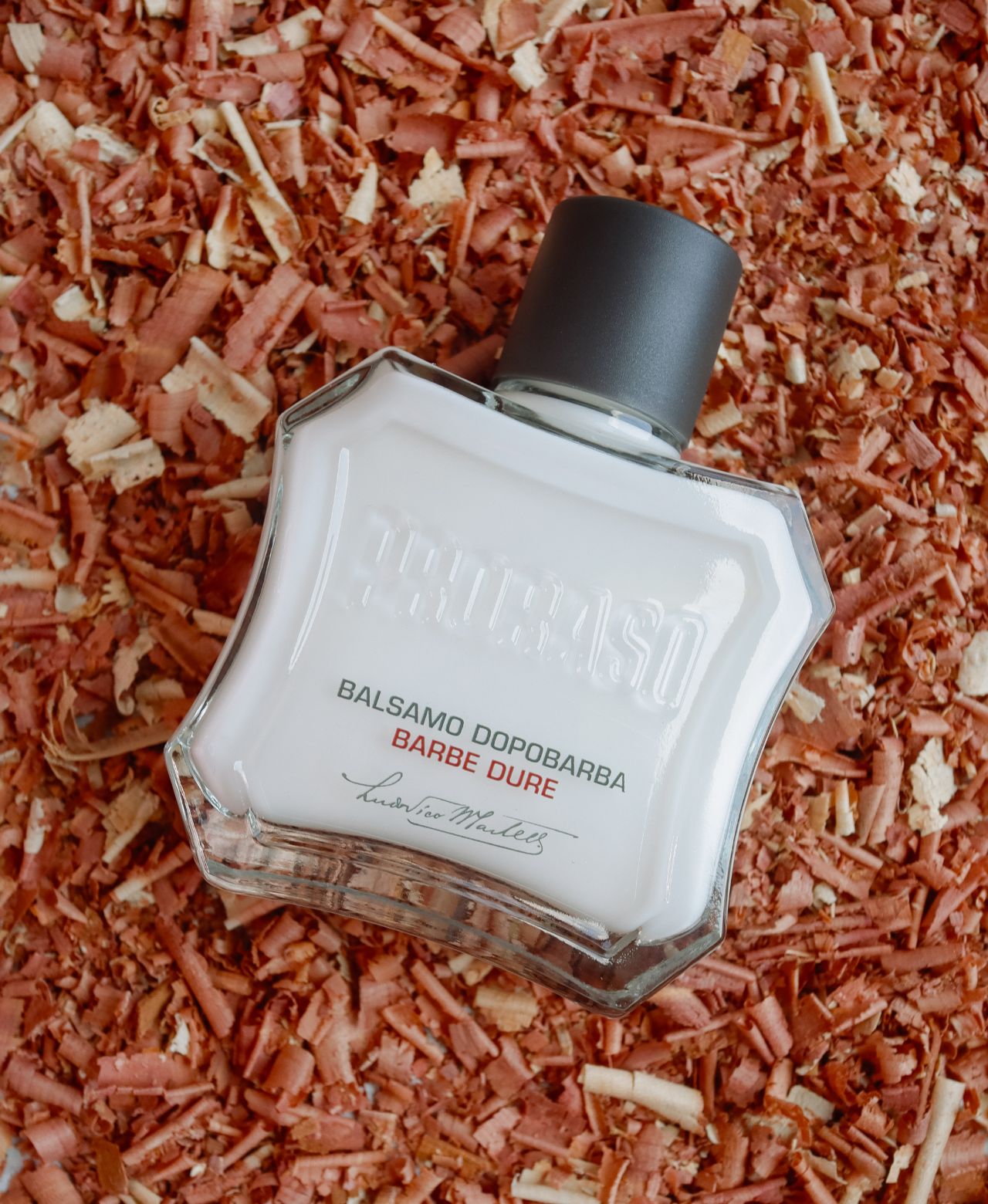 Tube of Coarse Beard After Shave Balm on sandalwood shavings on a grey table