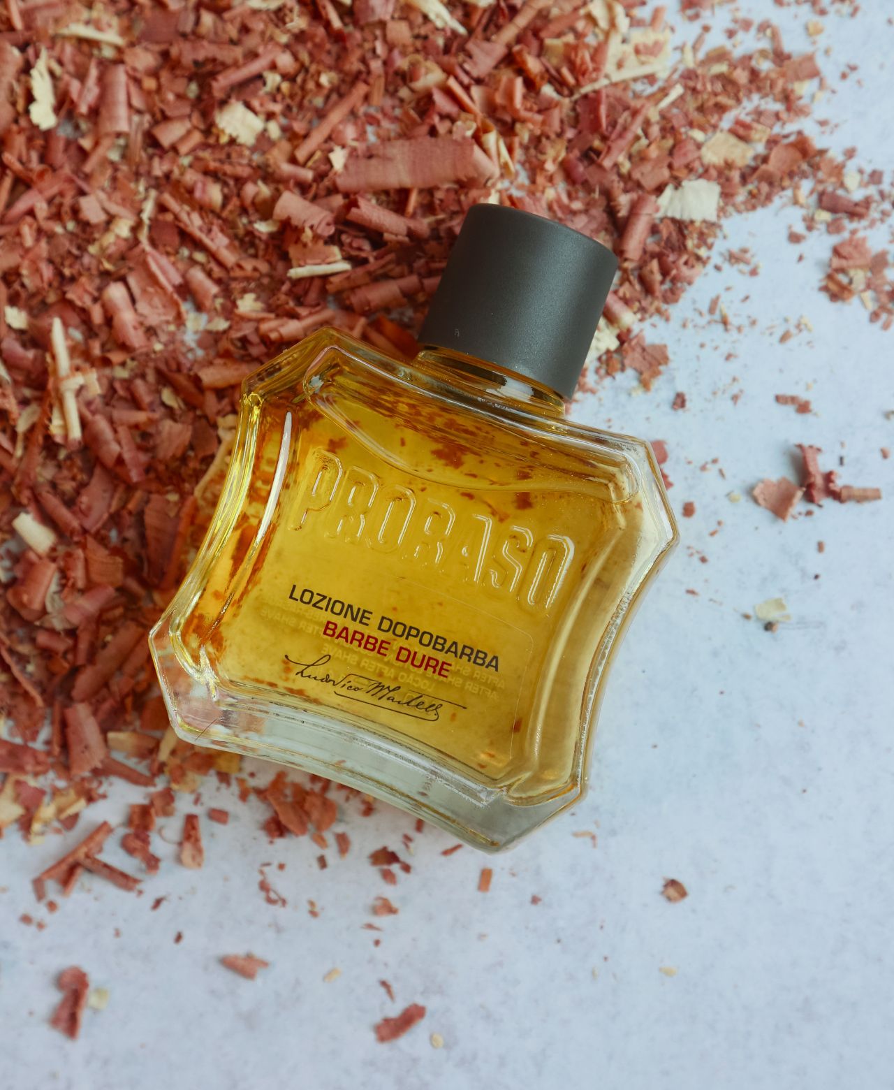 Bottle of Coarse Beard After Shave Lotion on sandalwood shavings on a grey table