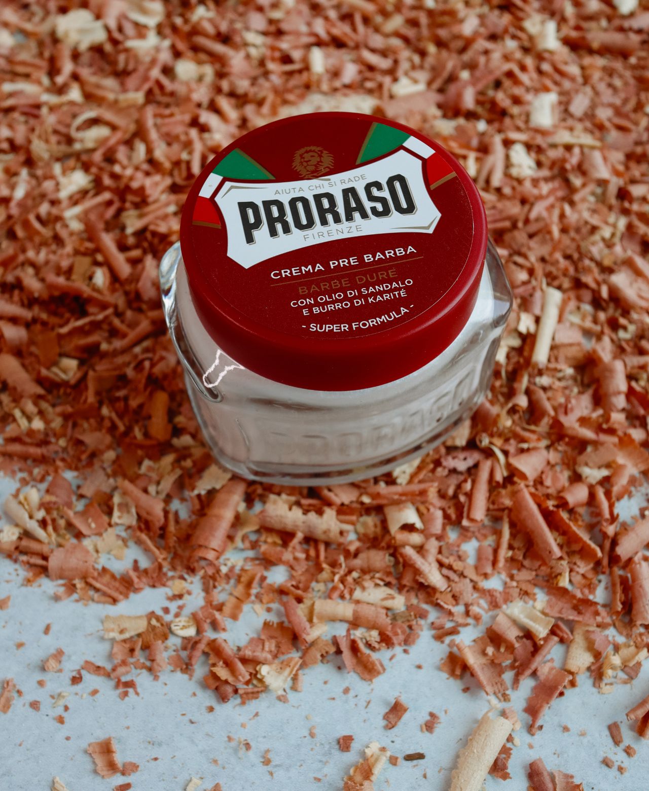 Jar of Coarse Beard Pre-Shave Cream sitting on shavings of sandalwood on a grey table
