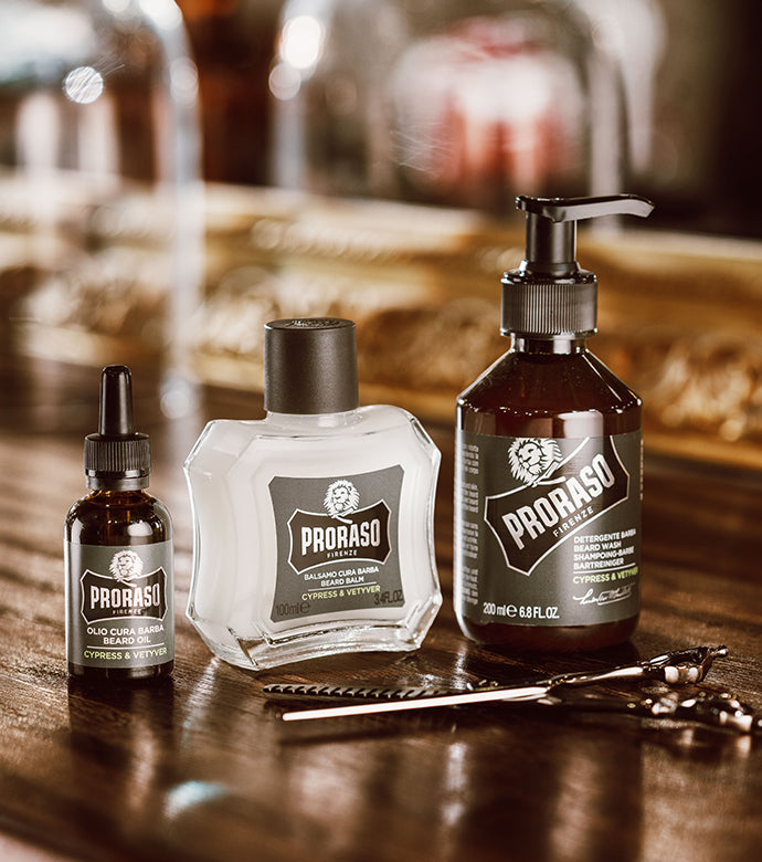 From left to right Cypress & Vetyver Beard Oil, Beard Balm and Beard Wash with a pair of scissors in front on a dark wood table