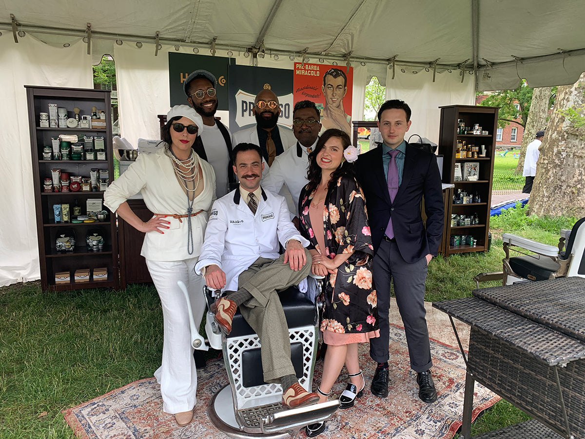 Left to right woman dressed in vintage, two men dressed in vintage and woman dressed in vintage stand behind Proraso Master Barber Michael Haar sitting in a barber chair outside
