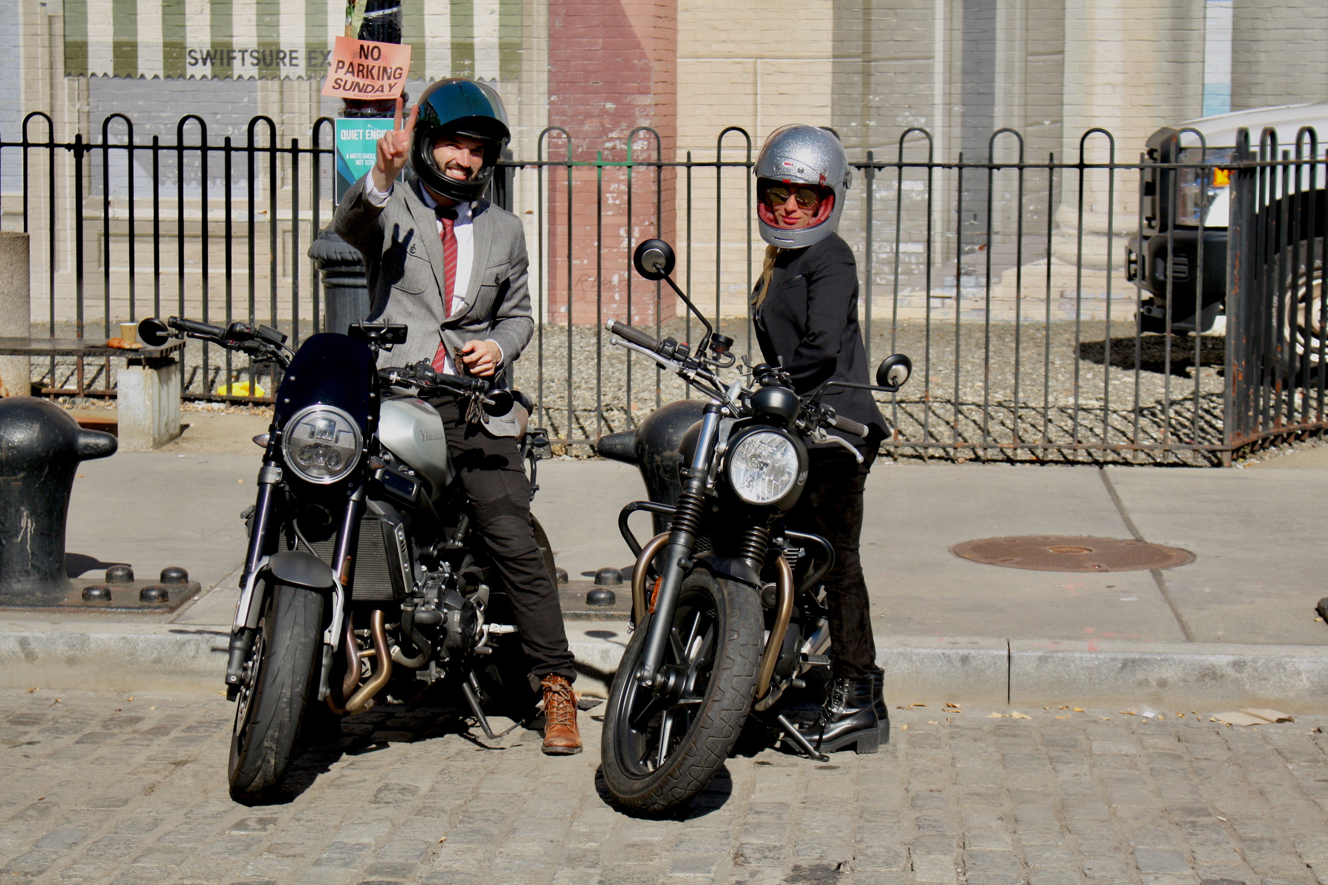 Man and woman dressed in vintage clothing posing on and next to their motorcycles