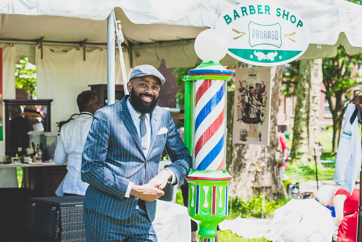 Proraso team member dressed in a suit standing in front of a vintage barber pole outside