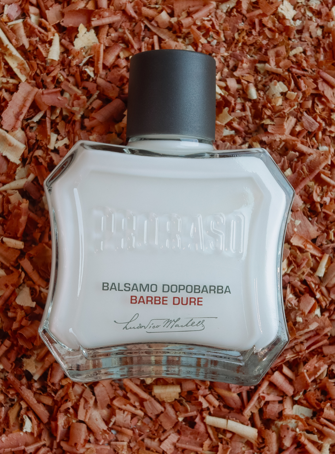 Bottle of Coarse Beard After Shave Lotion sitting on bed of Sandalwood chips