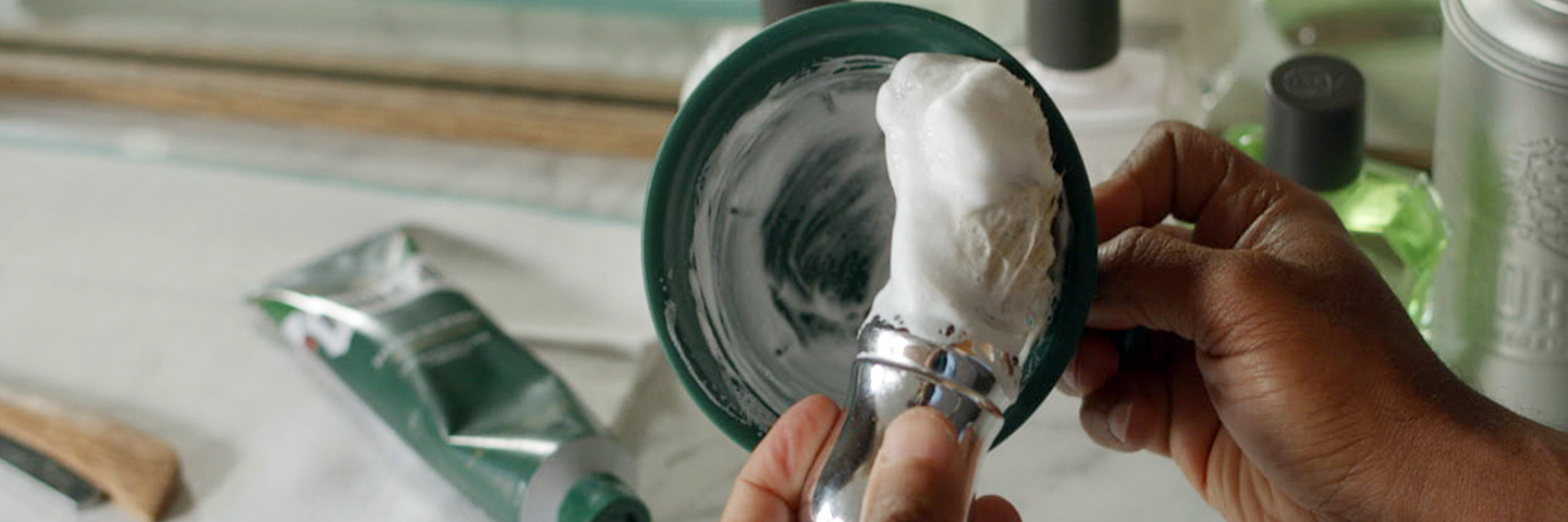 Man creating a thick lather with our Professional Shave Brush in a green bowl over a barber station