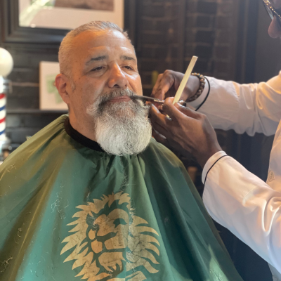 Man with long, thick beard and major moustache getting it groomed in a barber chair