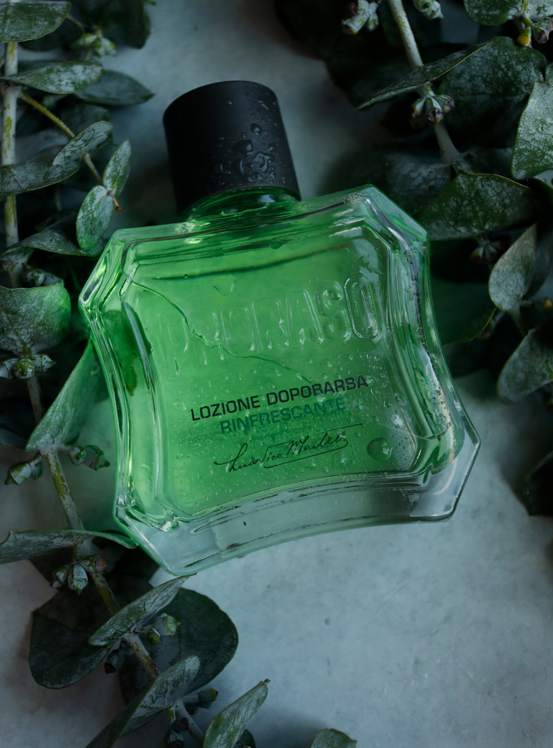 Bottle of Refreshing After Shave lotion on a grey table with strands of Eucalyptus laying around it