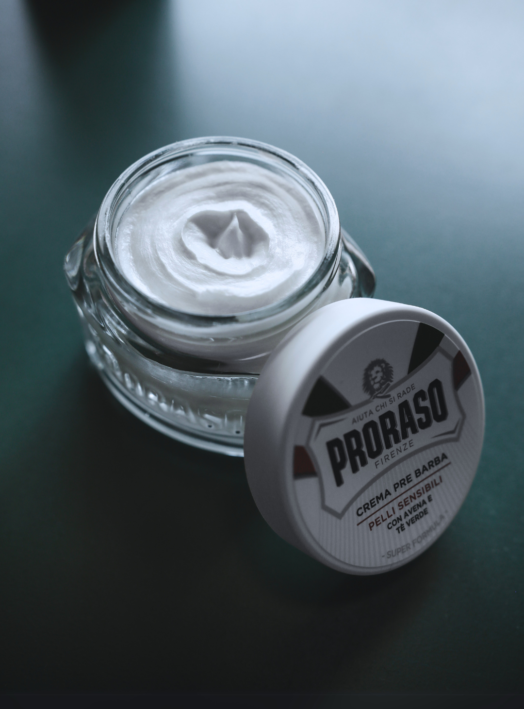 Jar of Sensitive Formula Pre-Shave Cream open with lid sitting in front on a dark table 